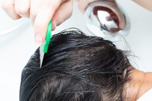 A stainless-steel fine-tooth nit comb being drawn through wet, conditioner-coated hair during a professional head lice treatment, the decision-moment of choosing a comb that actually clears the eggs.