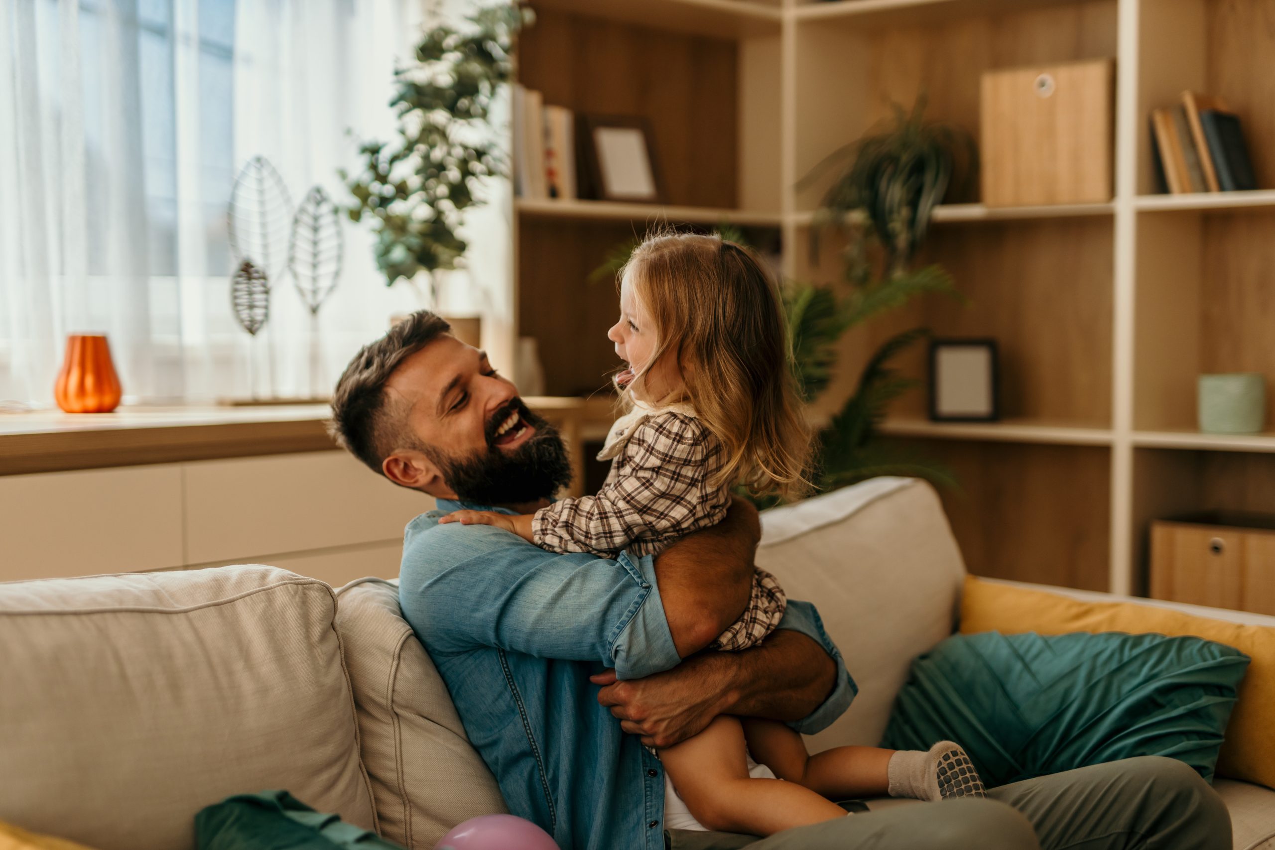 A bearded father sits on a sofa embracing his laughing daughter, the kind of close-contact moment a Mt Pleasant parent asks about when a child is diagnosed with head lice and the dad wonders whether his beard needs treatment too.